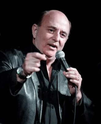 Scott Record on stage in a leather jacket, pointing into the audience mid-line